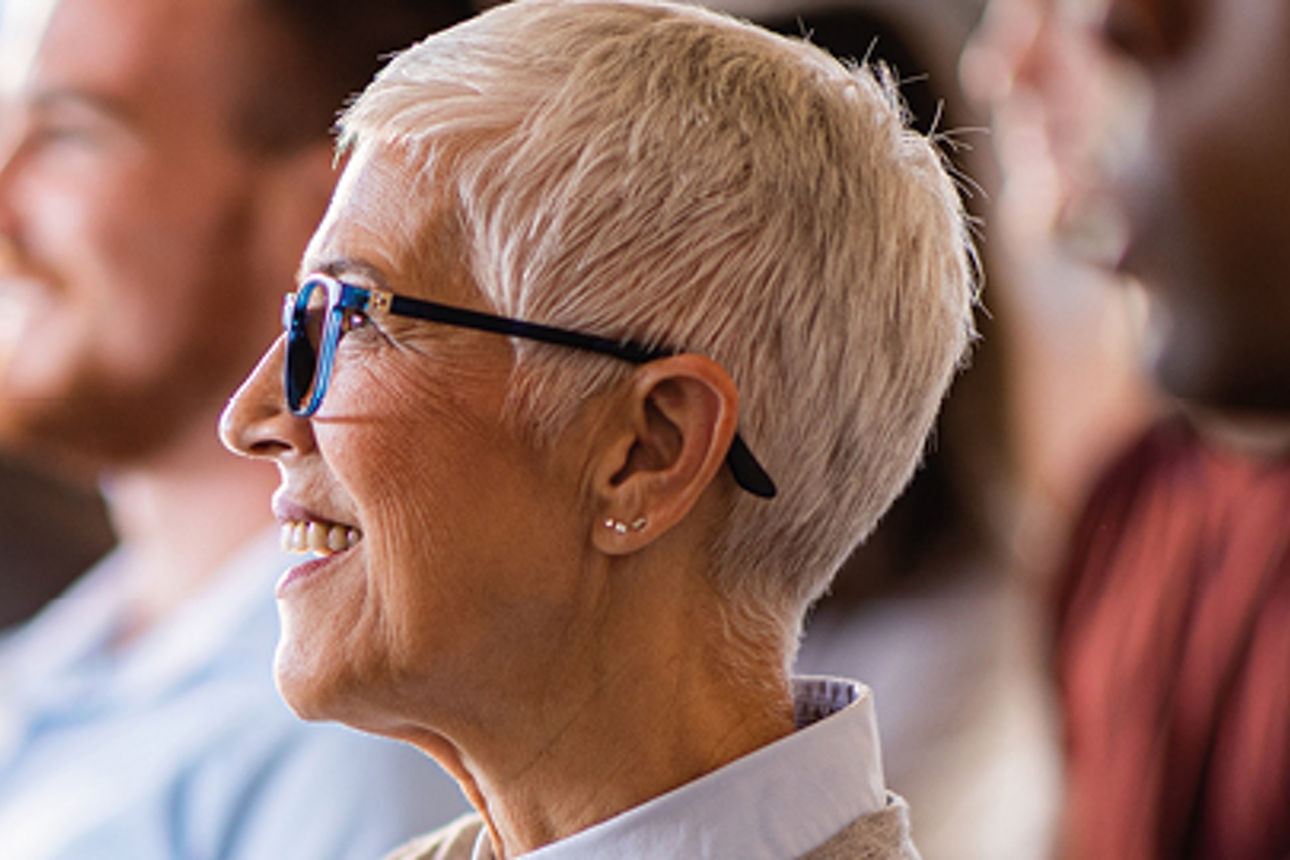 Eine ältere Frau sitzt lächelnd im Publikum