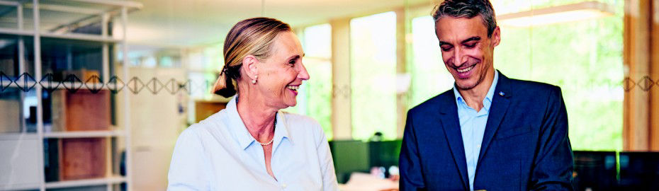 Ein Mann und eine Frau stehen in einem hell erleuchteten Büroraum und führen ein Gespräch.