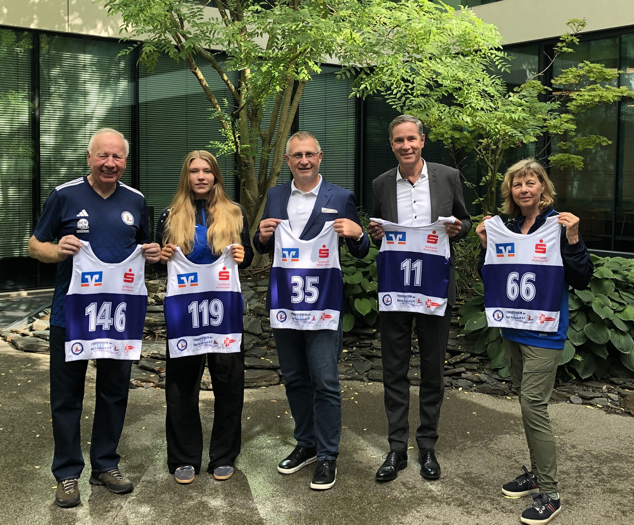 Fünf Personen mit je einem Startnummer-Leibchen in der Hand vor einem Baum.