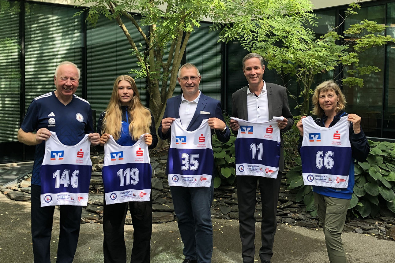 Fünf Personen mit je einem Startnummer-Leibchen in der Hand vor einem Baum.