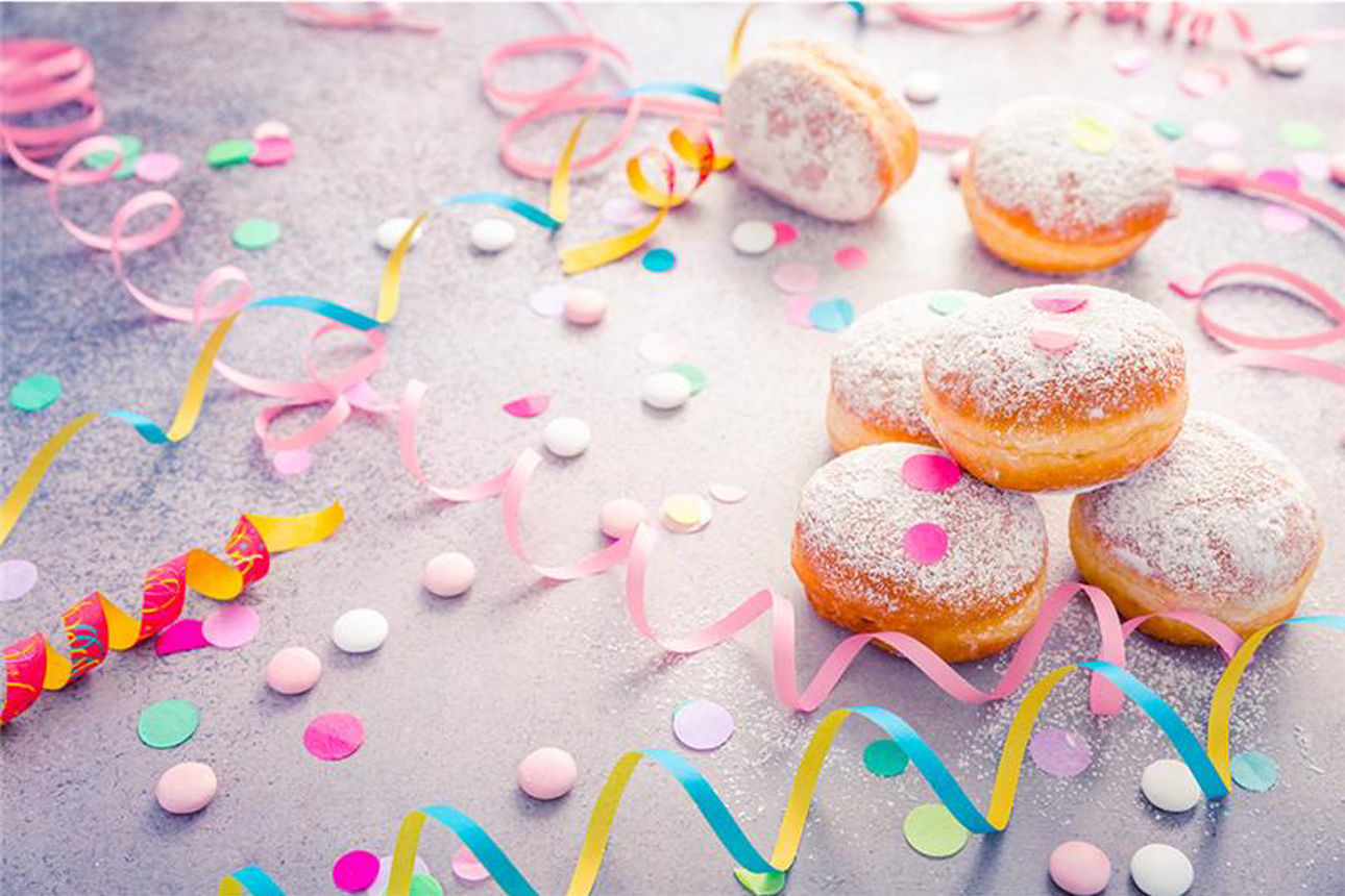 Berliner, Luftschlangen und buntes Konfetti liegen auf einem hellen Tisch
