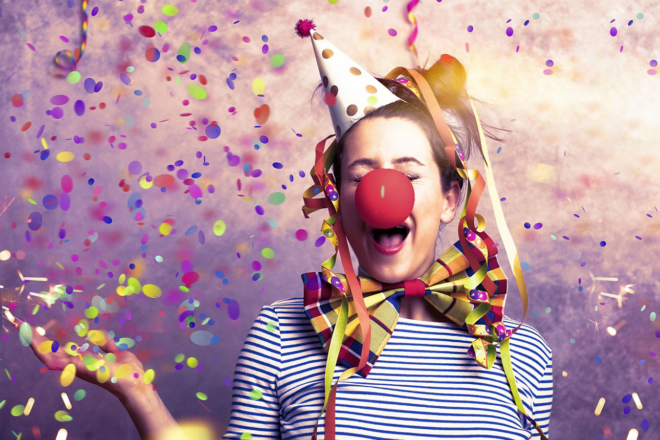 Person mit Karnevalshut, bunter Fliege und Konfetti feiert ausgelassen Karneval.