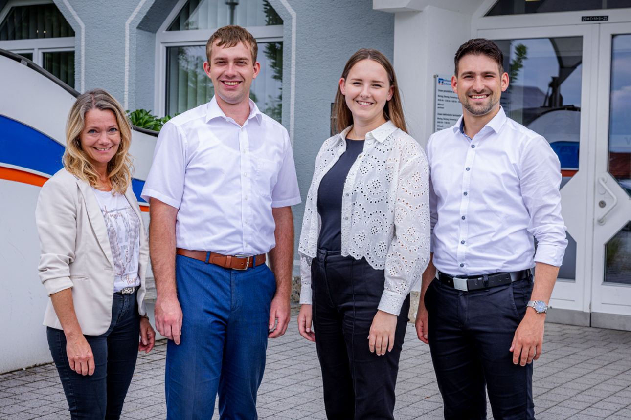 Eine Gruppe von jungen Personen in Business Kleidung steht vor einer Bankfiliale.