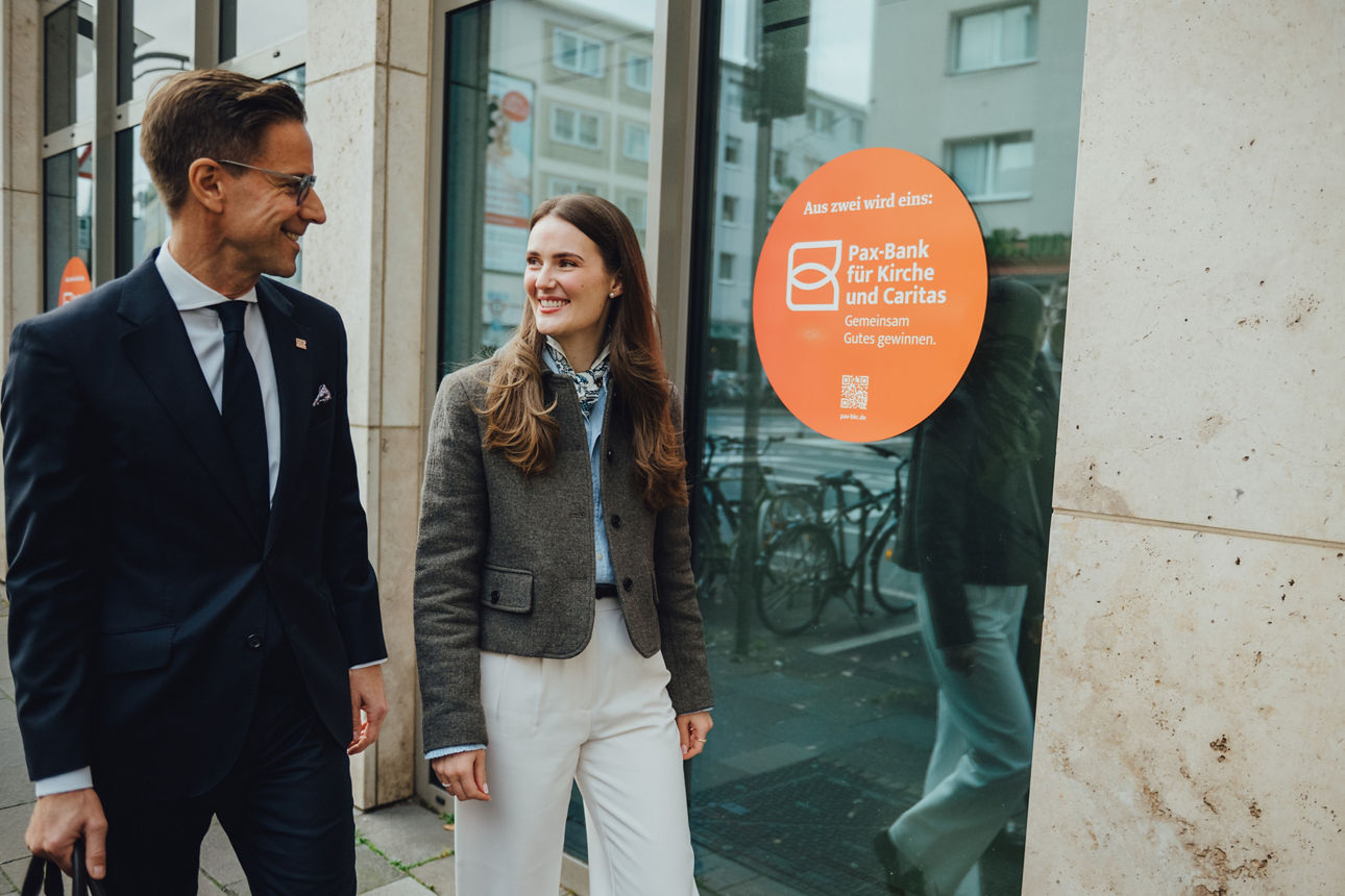 Zwei Personen laufen an einem Gebäude vorbei und unterhalten sich