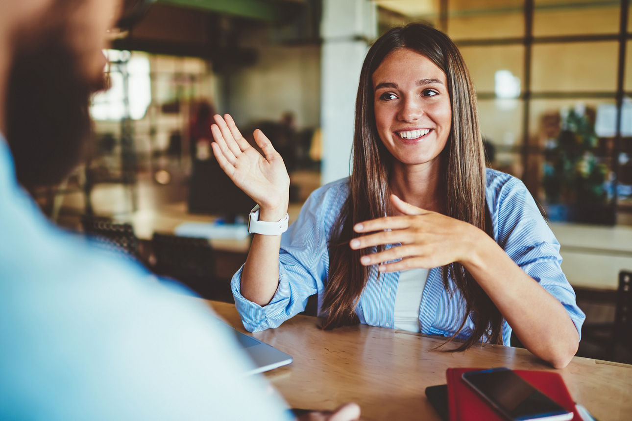 Glückliche junge Frau, die einem vor ihr sitzendem Mann etwas erklärt.