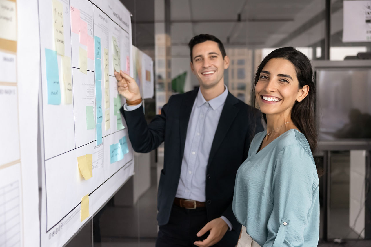  Zwei glückliche Geschäftskollegen stehen zusammen am Scrum Board