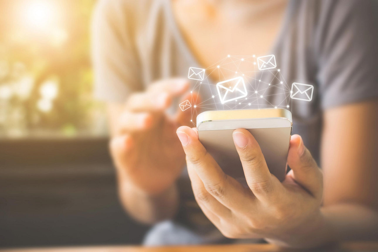 Eine Frau hält ihr Smartphone in der Hand, darüber zu sehen sind Briefumschläge, die eingehende E-Mails darstellen sollen.