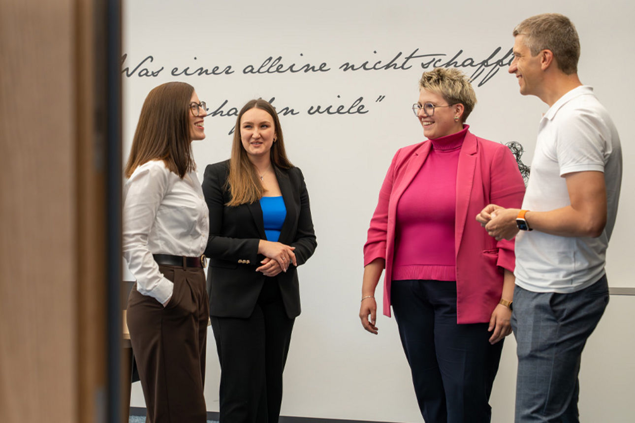 Vier Menschen stehen in einem Konferenzraum zusammen und sprechen miteinander