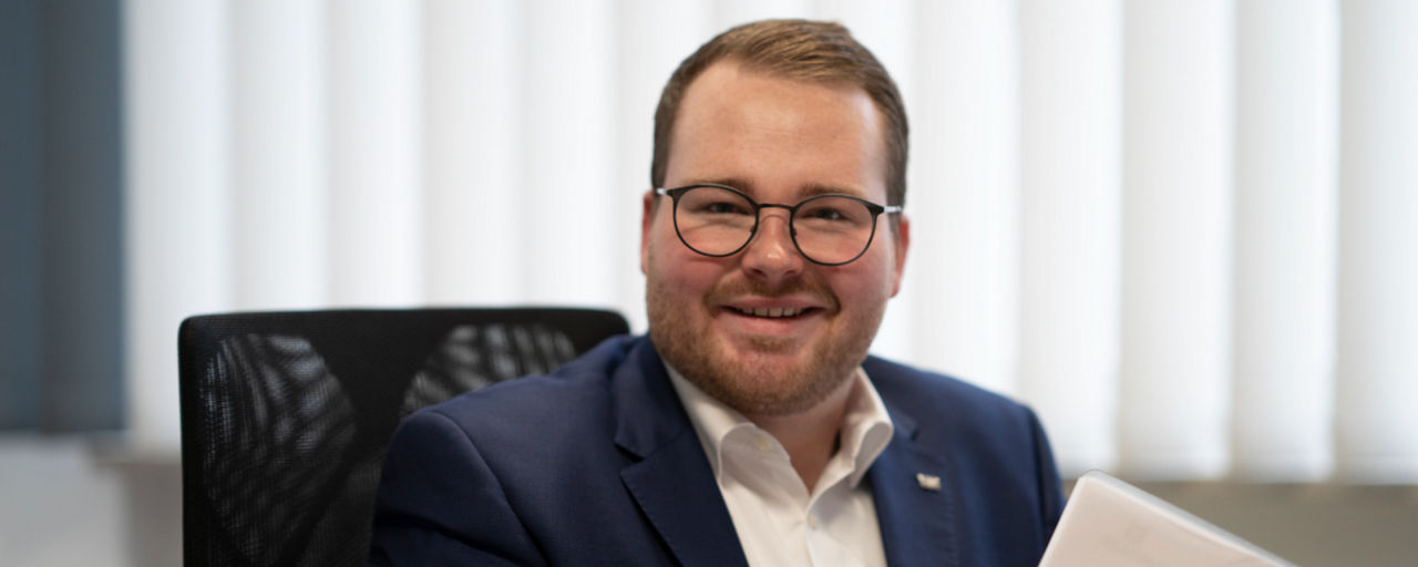 Ein lächelnder Mann sitzt an seinem Arbeitsplatz.