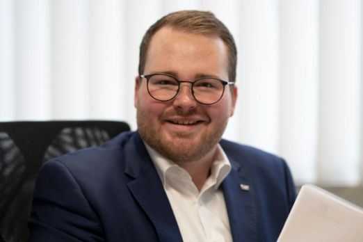 Ein lächelnder Mann sitzt an seinem Arbeitsplatz.