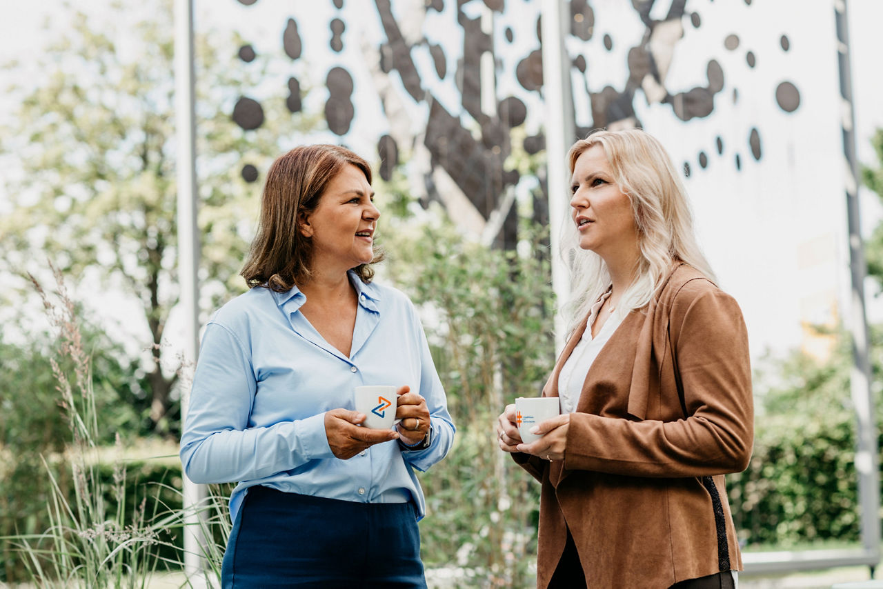 Abbildung zeigt zwei Mitarbeiterinnen von Meine Bank, welche sich in der Kaffeepause unterhalten