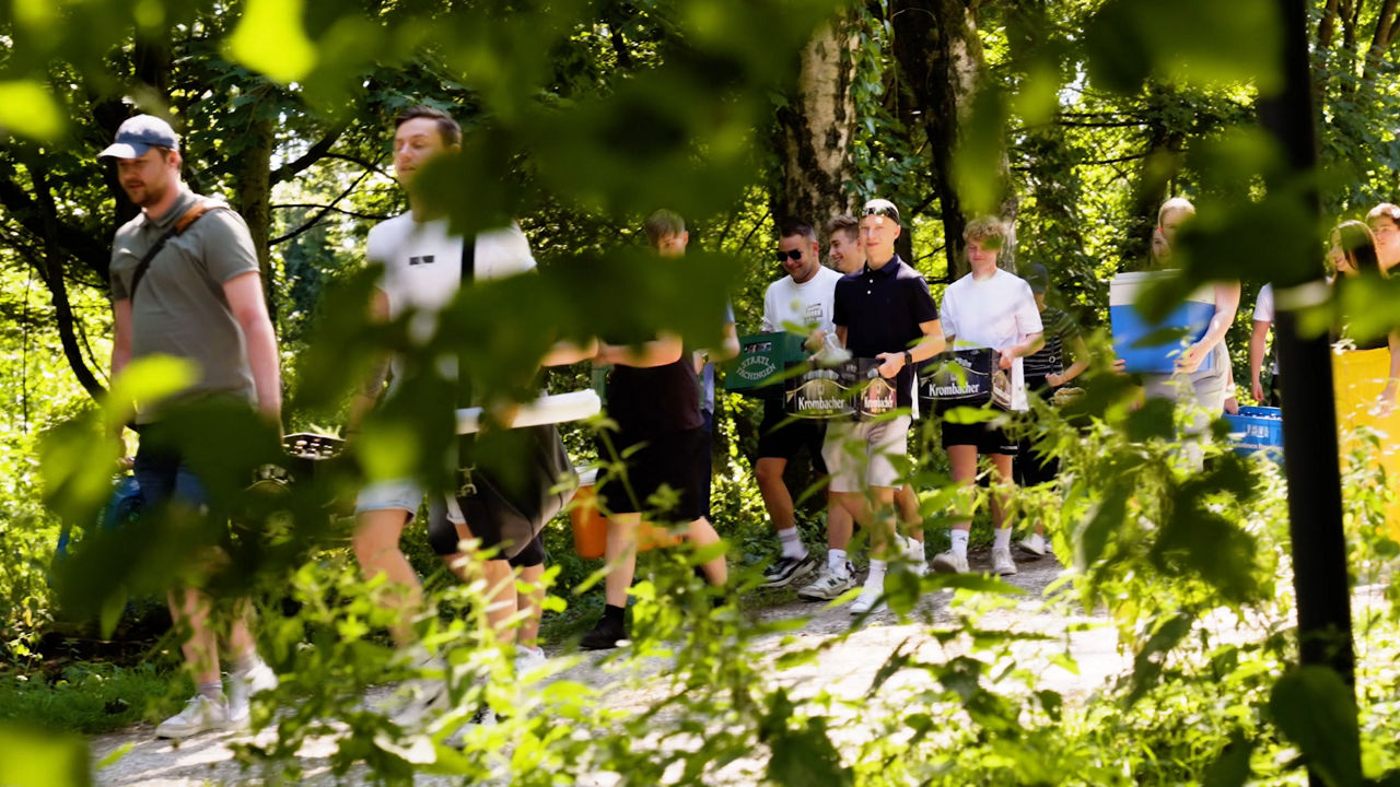 Die Auszubildenden tragen die Kisten und Kühlboxen für den gemeinsamen Ausklang durch den Wald.