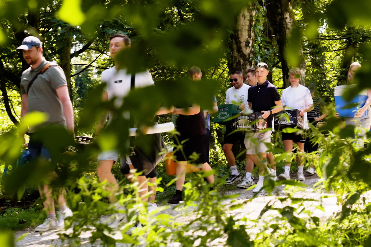 Die Auszubildenden tragen die Kisten und Kühlboxen für den gemeinsamen Ausklang durch den Wald.