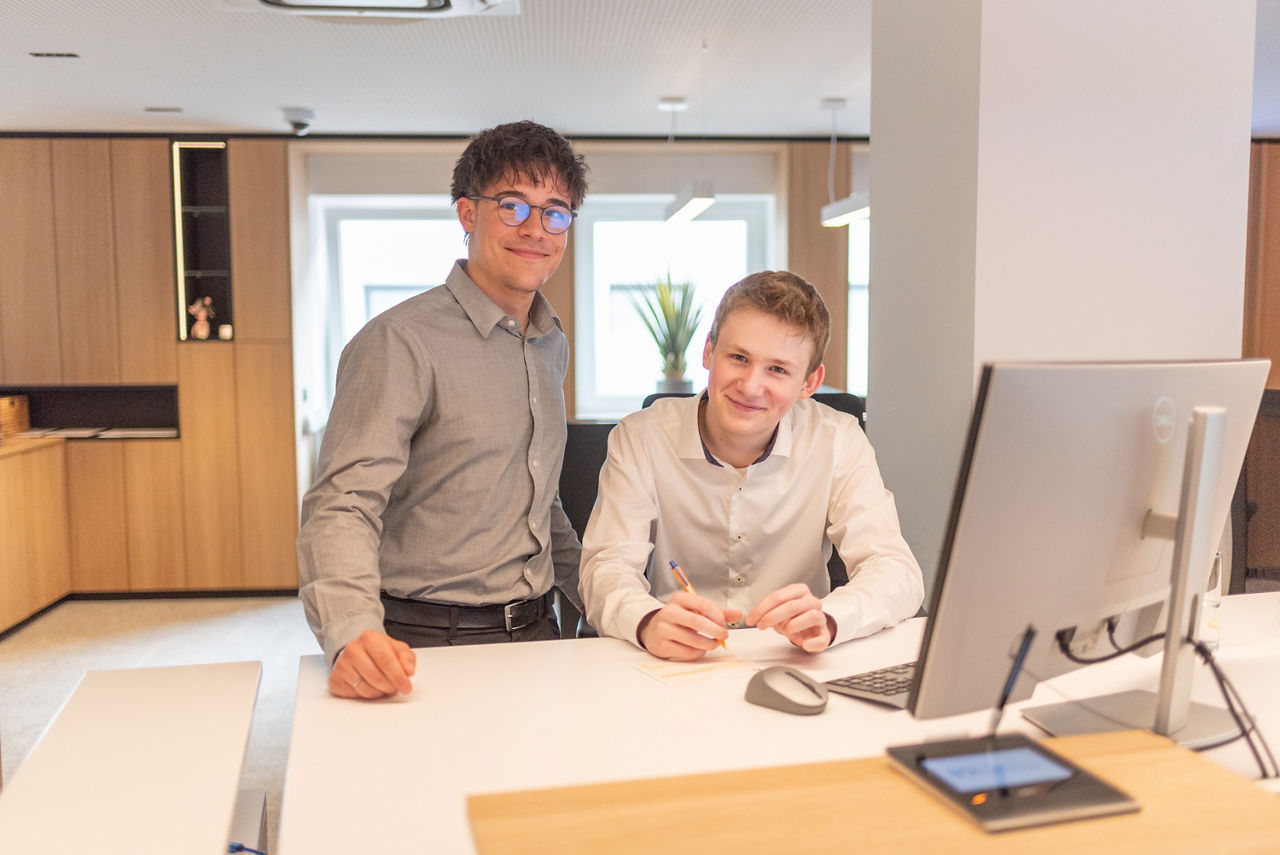 Zwei junge Männer stehen im Servicebereich der Bank vor einem Computerr