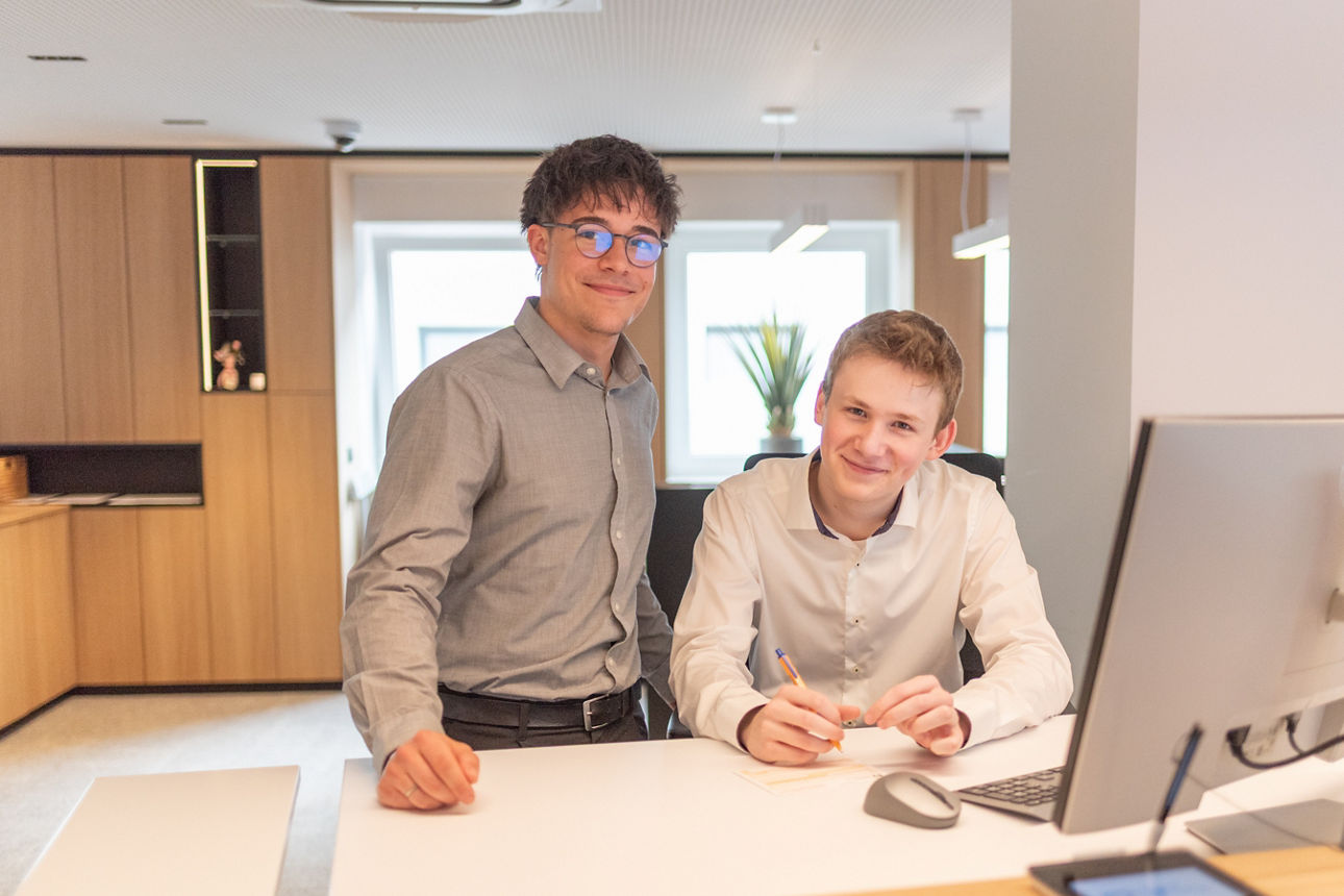 Zwei junge Männer stehen im Servicebereich der Bank vor einem Computerr