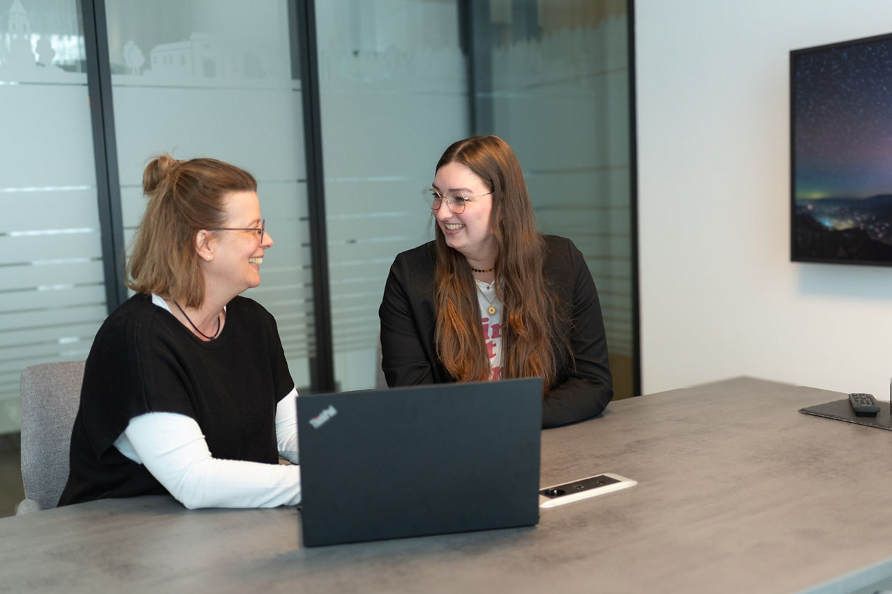 Zwei Frauen lächeln vor einem Laptop sitzend