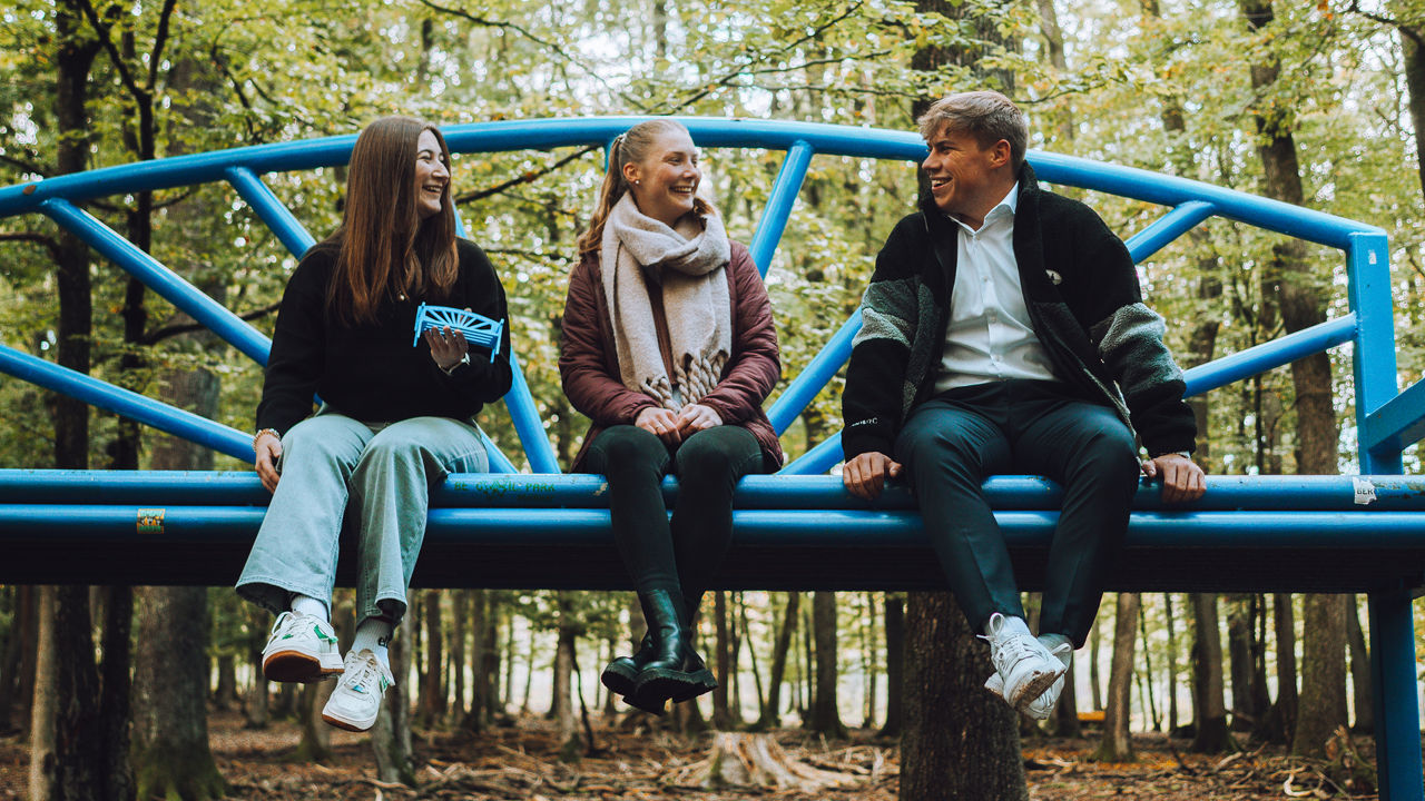 Drei junge Menschen sitzen auf einer großen blauen Bank im Wildpark