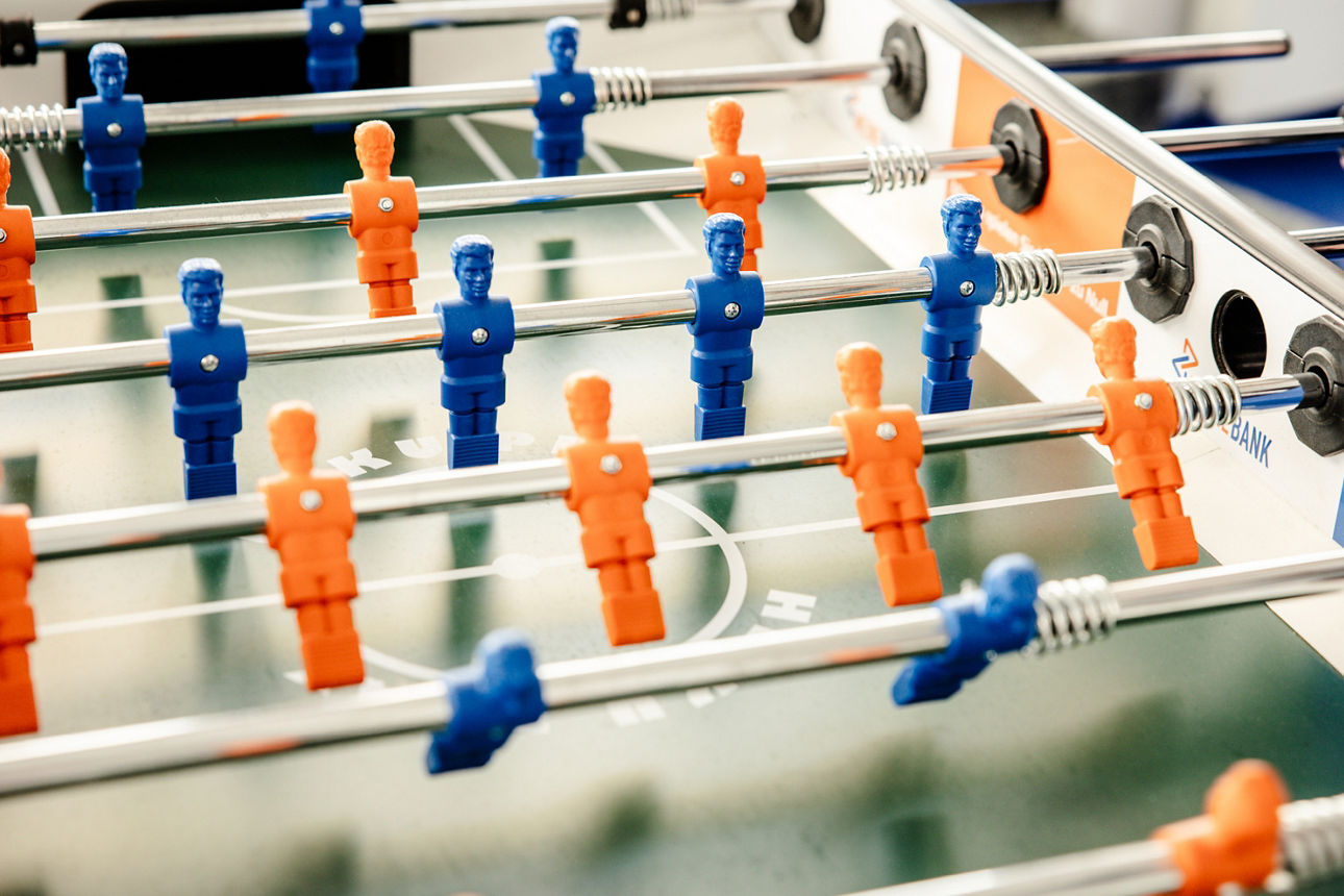 Abbildung zeigt einen Tischkicker mit orangenen und blauen Spielern