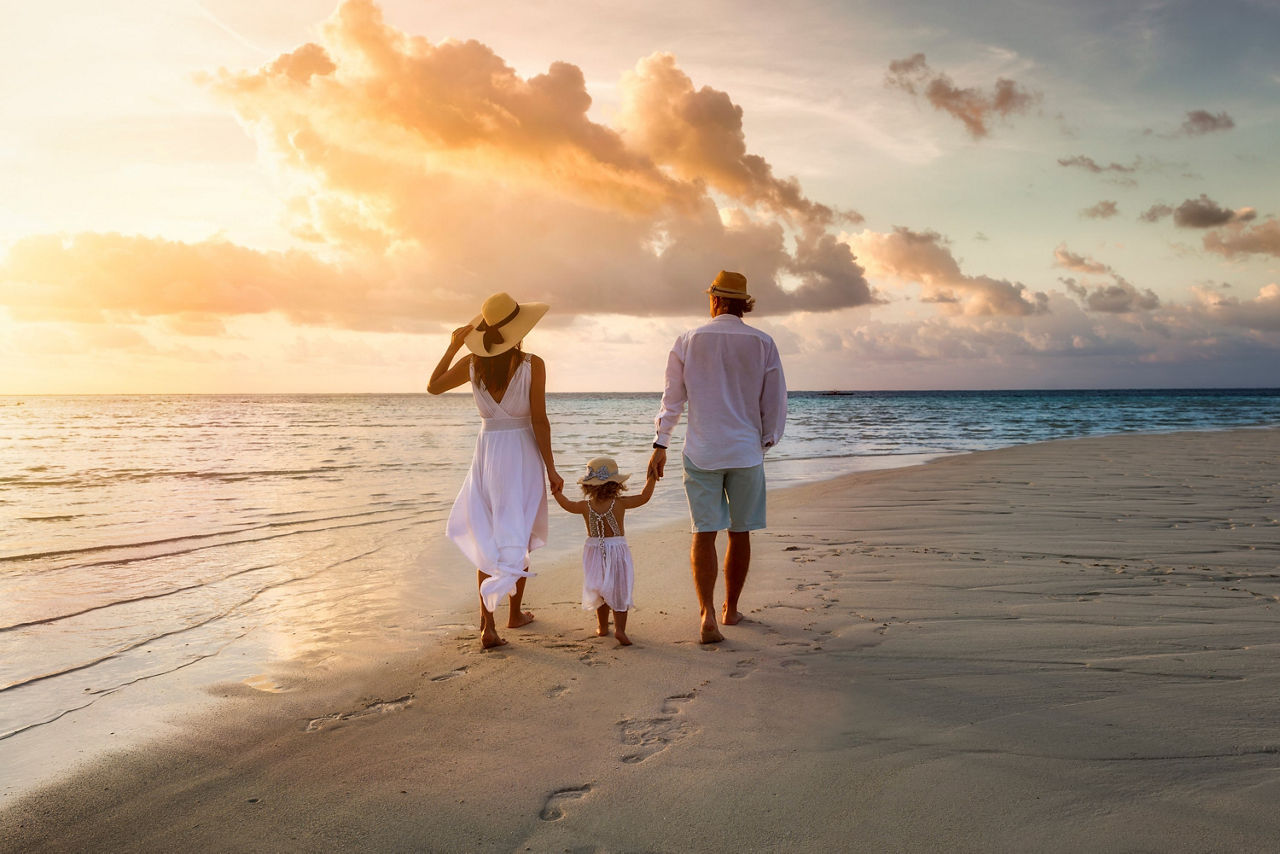 Ein Paar mit Kind läuft zusammen am Strand im Sonnenuntergang. Sie sind von hinten zu sehen.