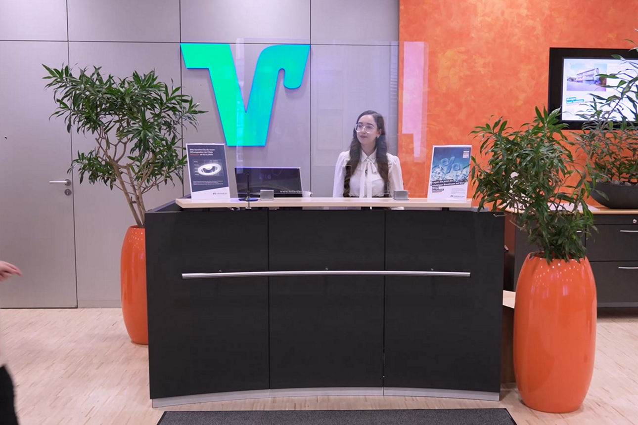 Junge Frau sitzt hinter einem Bankschalter wo eine Kundin hinläuft