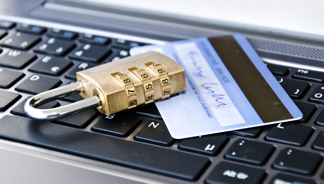 Auf einer Laptoptastatur liegen eine Bankkarte und darauf ein Vorhängeschloss