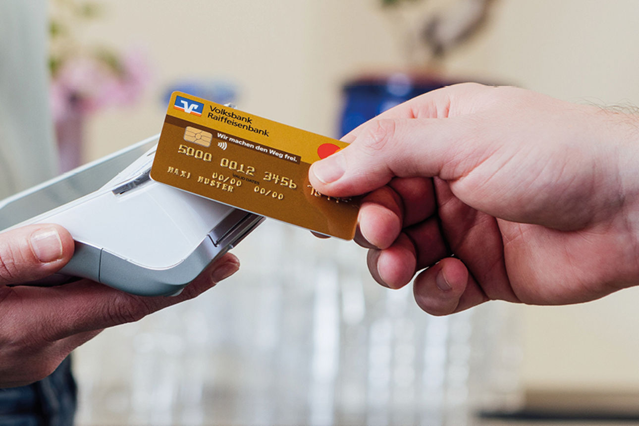 Eine Person hält ein Zahlungsterminal in Hand. Eine weitere Person legt die Karte zum zahlen auf das Terminal.