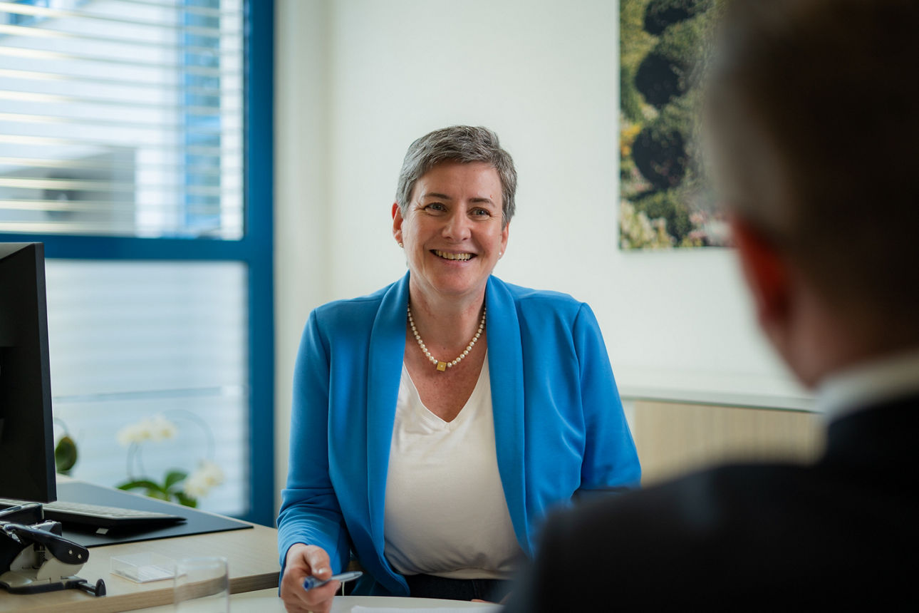 Eine lächelnde Dame sitzt in einem Büro vor einem Herren