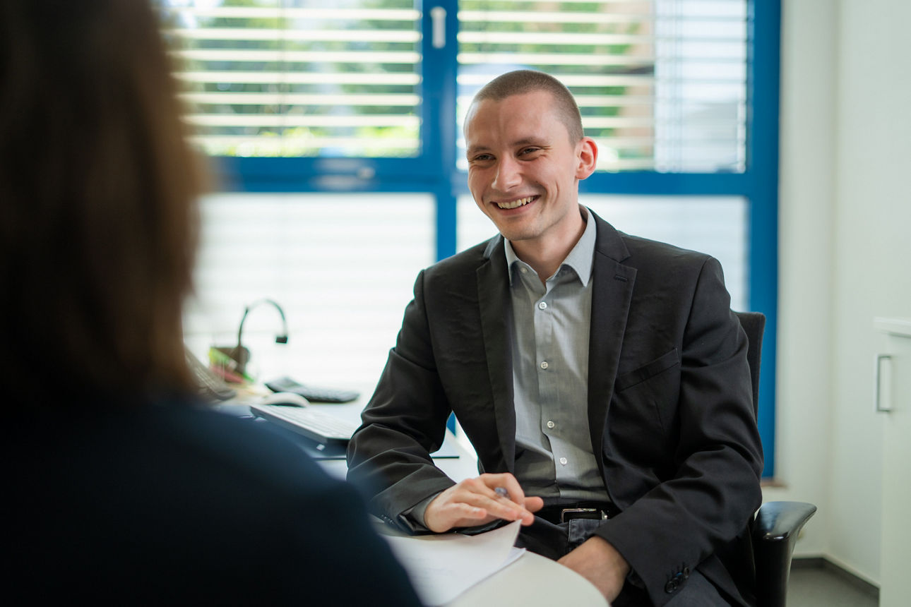 Ein lächelnder Herr sitzt in einem Büro vor einer Dame