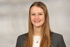 Lina Kau hat lange blonde Haare und trägt ein Businessoutfit in grau