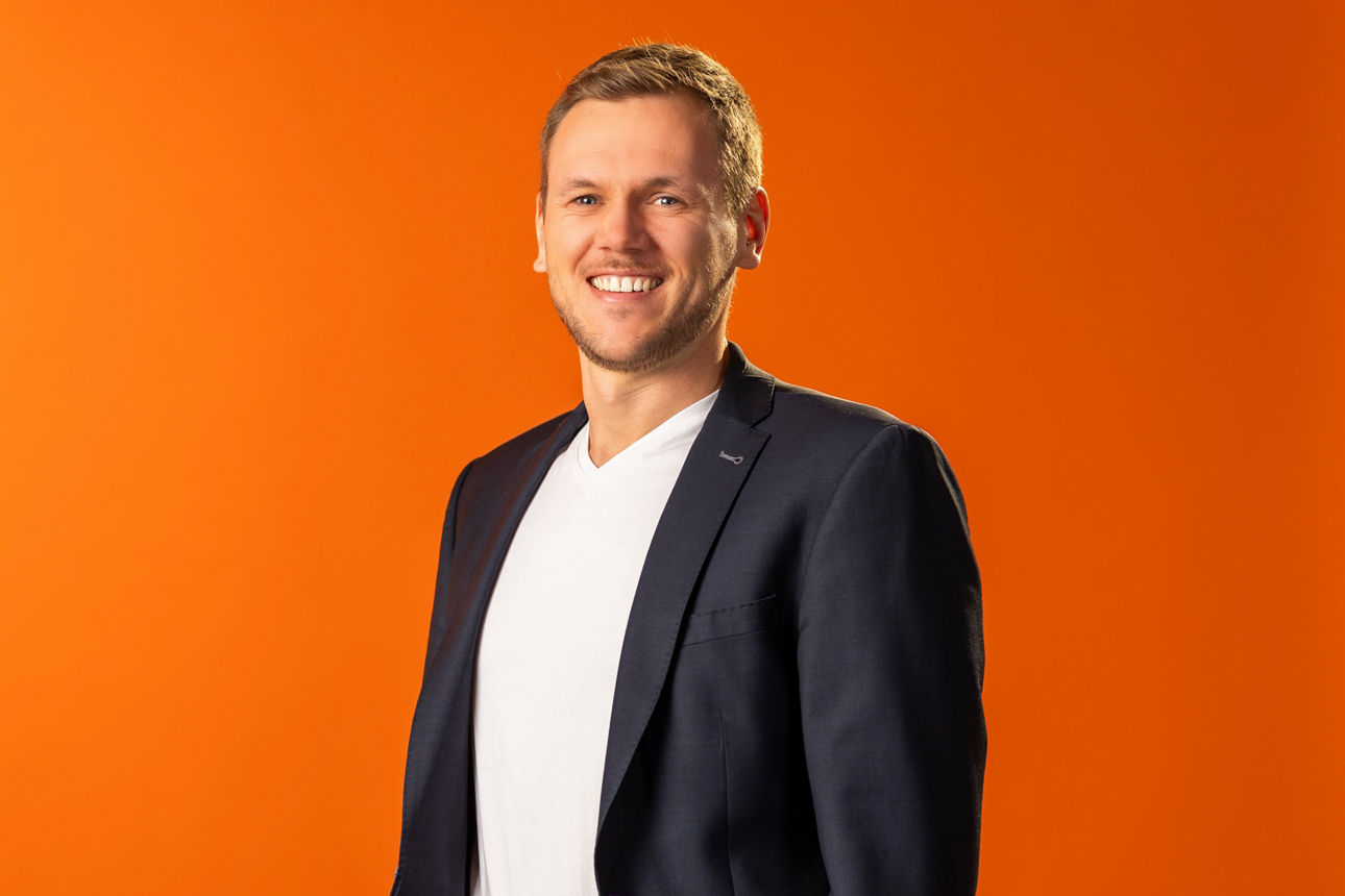 Bild unseres Mitarbeiters Michael Keller vor einer orangenen Wand