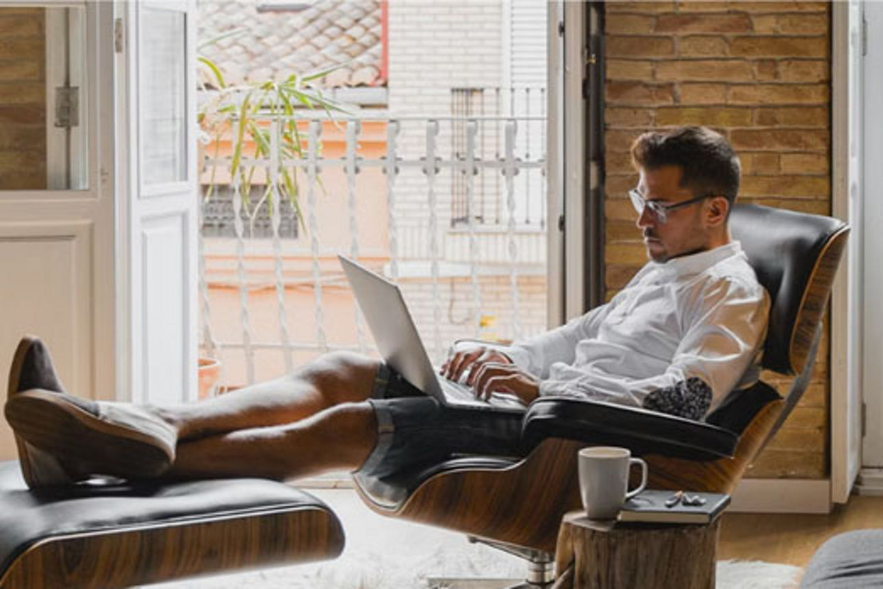 Mann sitzt auf einem Sessel und arbeitet am Laptop