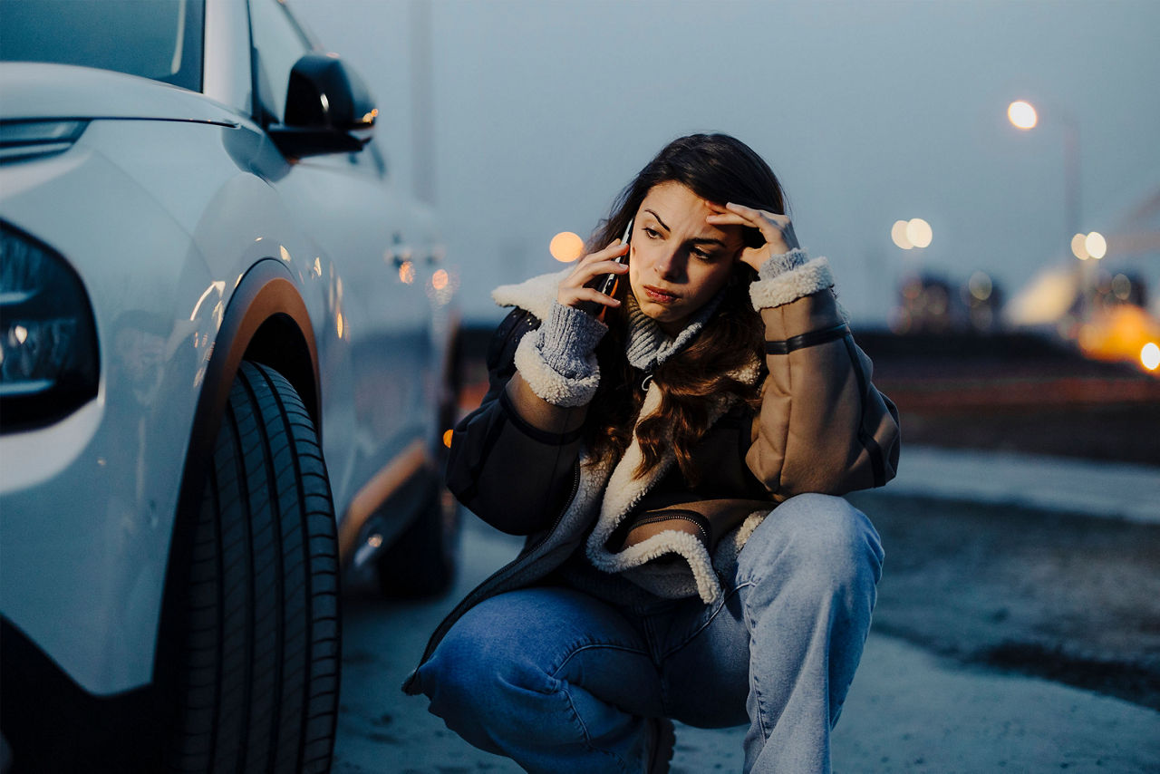 Frau sitzt vor ihrem Auto und telefoniert.
