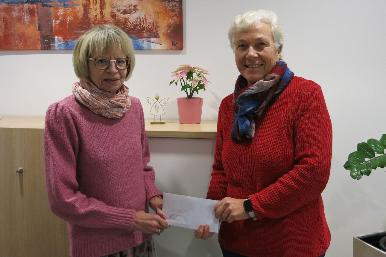 Zwei Frauen lächeln in die Kamera. Sie halten einen Briefumschlag in der Hand.