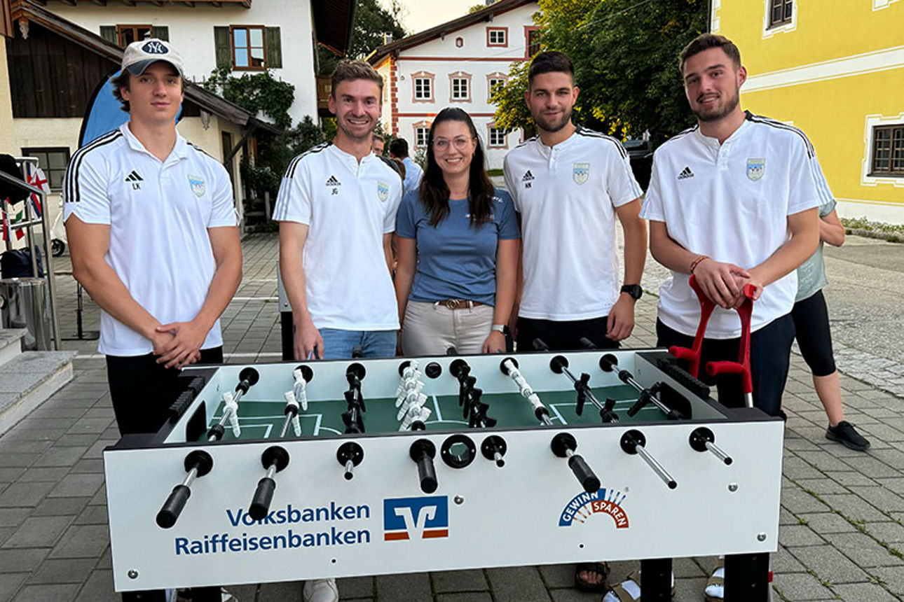 Gruppe von Menschen, die um einen Kickertisch herumstehen.