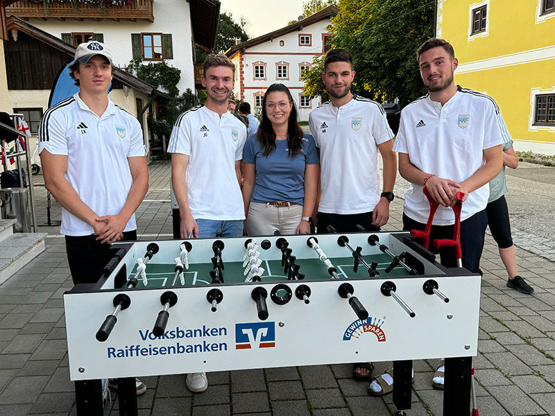 Gruppe von Menschen, die um einen Kickertisch herumstehen.