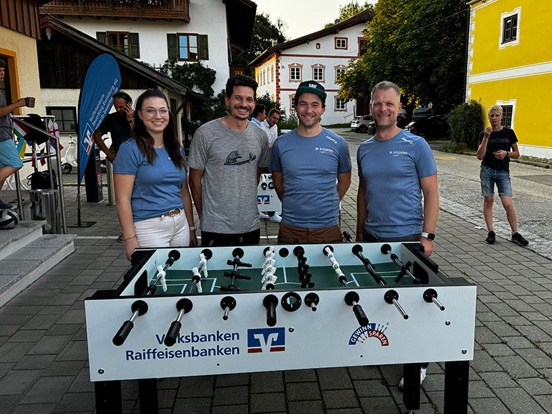 Gruppe von Menschen, die um einen Kickertisch herumstehen.