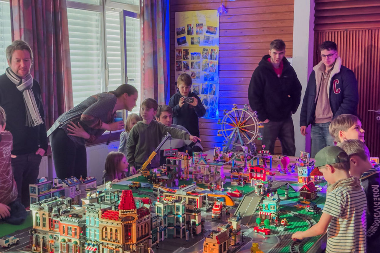 4 Erwachsene und eine Gruppe von Kindern vor einer Modellstadt mit Häusern und einem Riesenrad