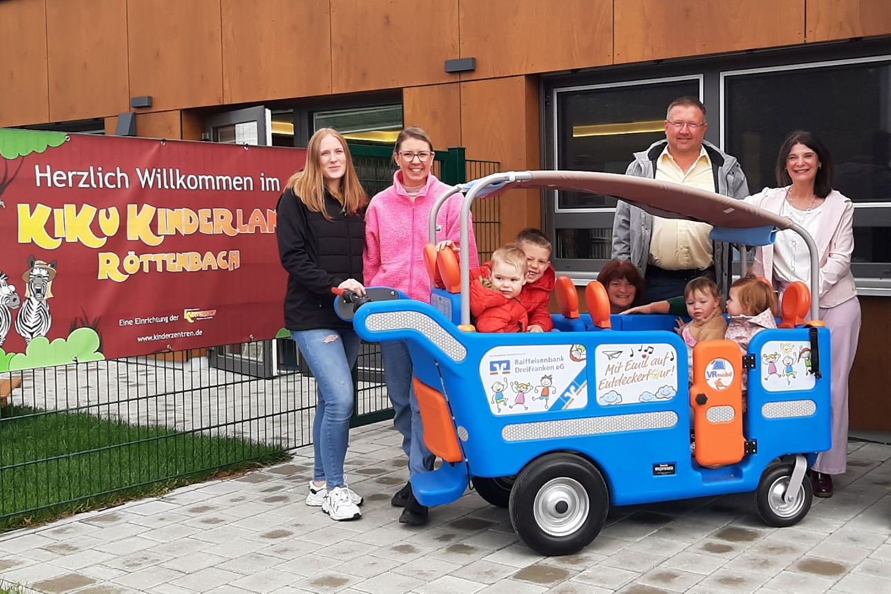 Mitarbeiter und Kinder der Kita KiKu Kinderland und Mitarbeiter der Bank posieren mit dem VRmobil