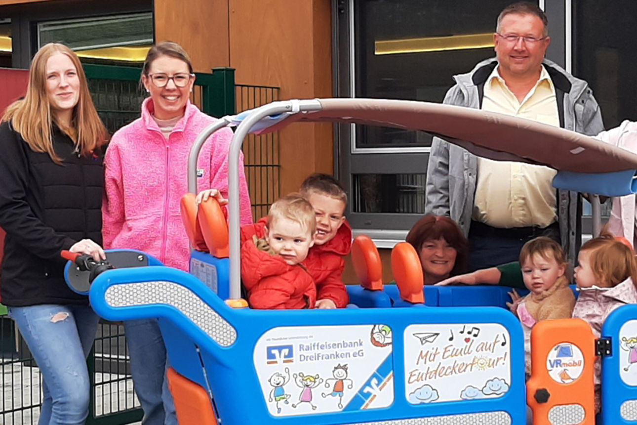 Mitarbeiter und Kinder der Kita KiKu Kinderland und Mitarbeiter der Bank posieren mit dem VRmobil