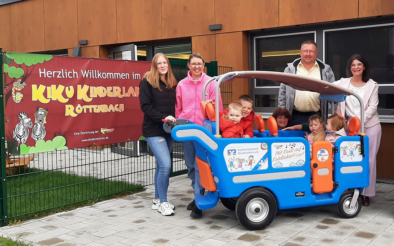Fröhliche Erwachesene und Kinder stehen beim VRmobil Emil.