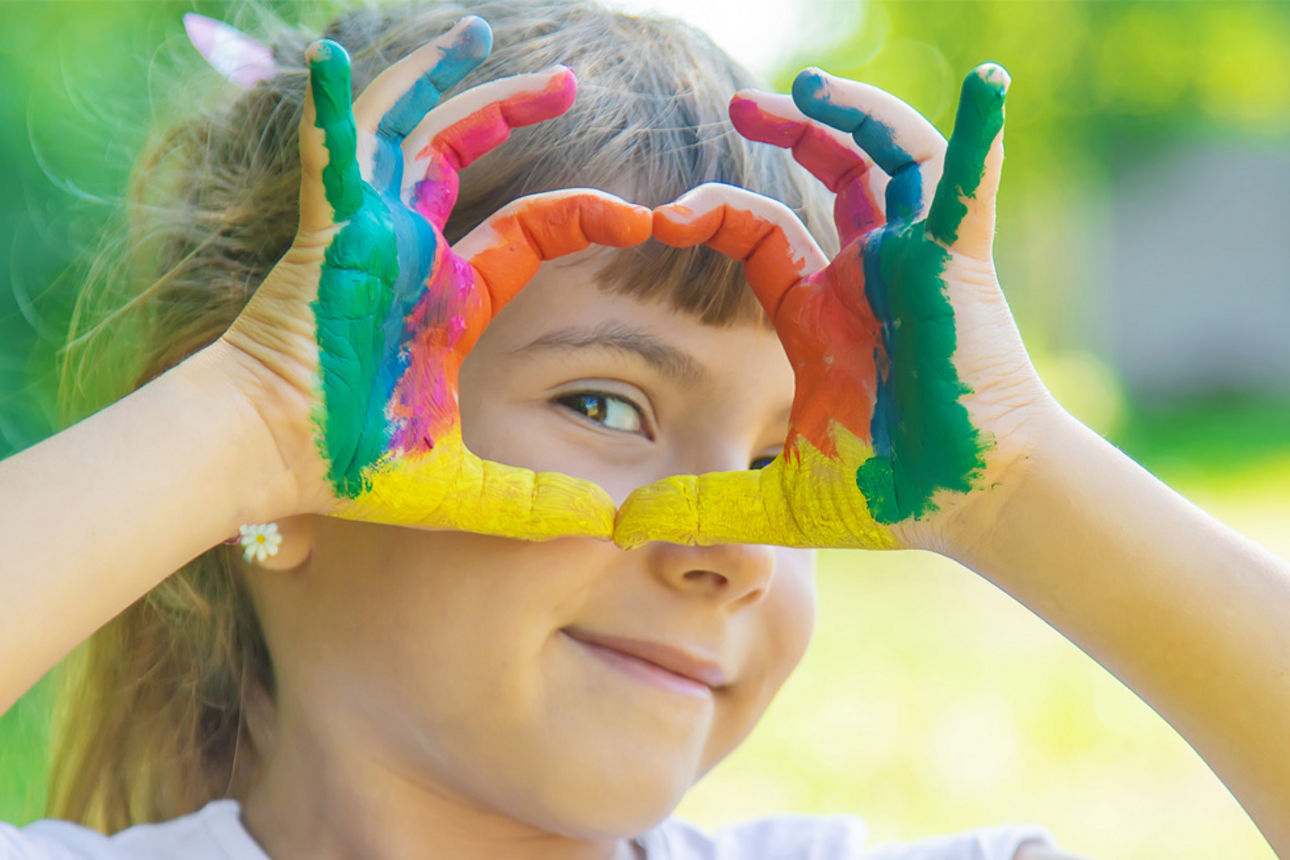 Mädchen zeigt mit ihren bunt gefärbten Fingern ein Herz