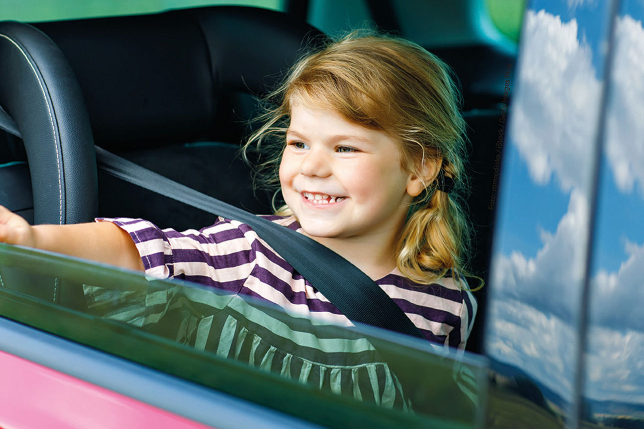 kleines Mädchen sitzt lächelnd im Auto und winkt aus dem Fenster