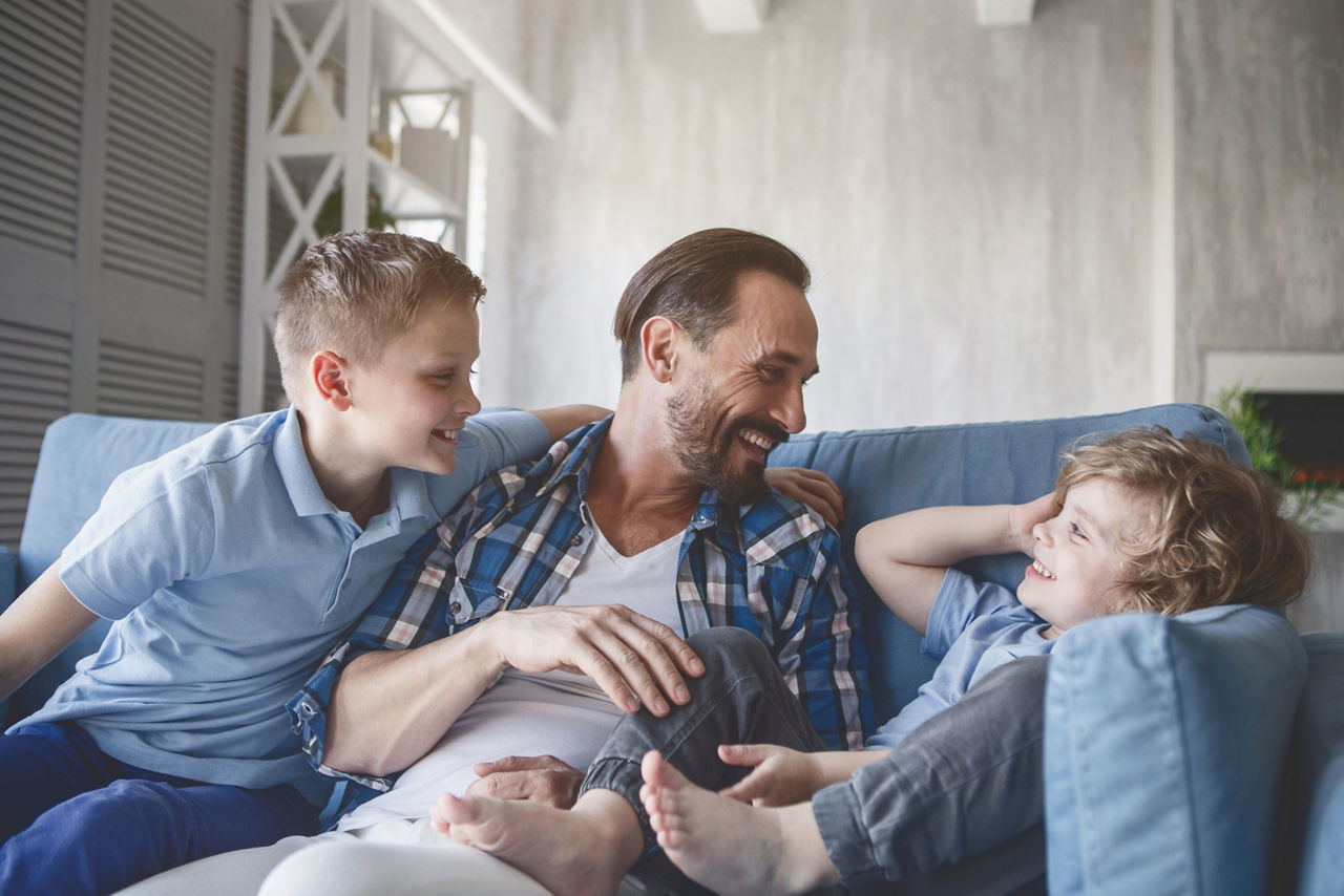 Vater sitzt mit zwei Kindern auf dem Sofa und albert herum