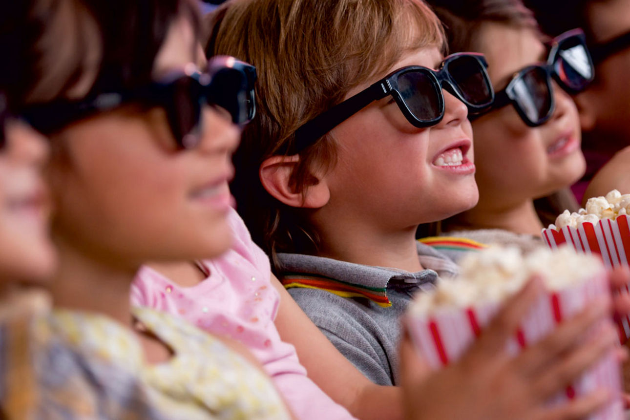 Kinder mit 3D-Brillen genießen Kinoerlebnis und Popcorn.
