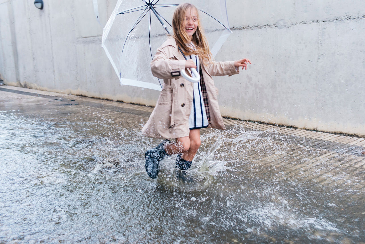 Kleines Mädchen hüpft mit Regenschirm durch eine große Pfütze