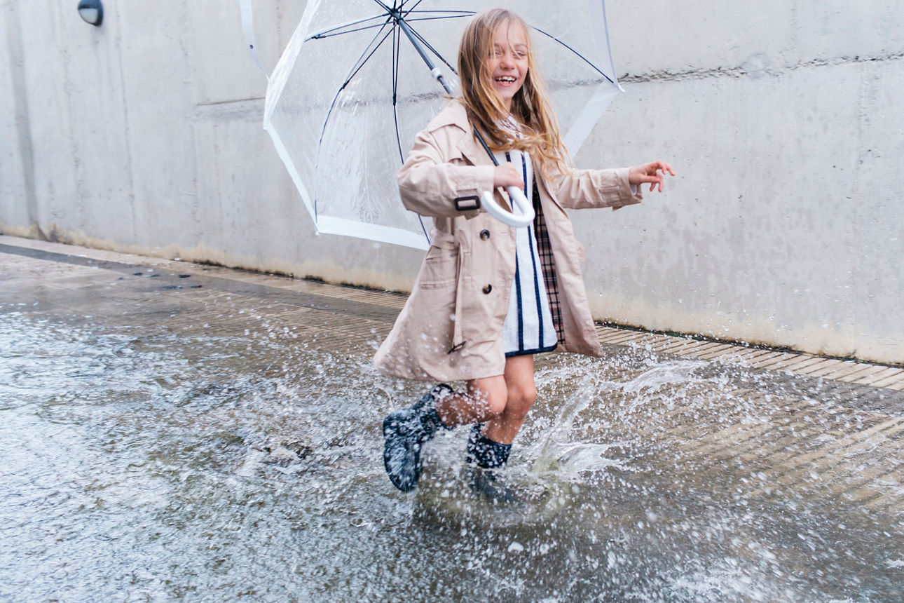 Kleines Mädchen hüpft mit Regenschirm durch eine große Pfütze