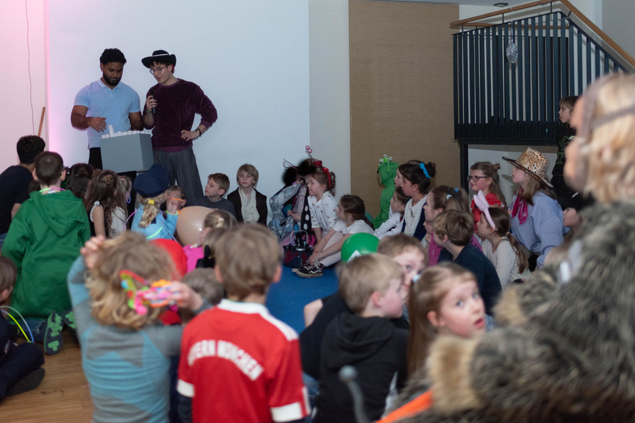 Verkleidete Kinder hören gebannt zwei jungen Erwachsenen zu.
