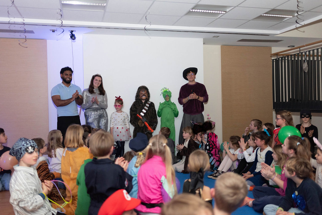 Drei verkleidete Kinder und drei verkleidete junge Erwachsenen stehen vor einer Gruppe von Kindern.