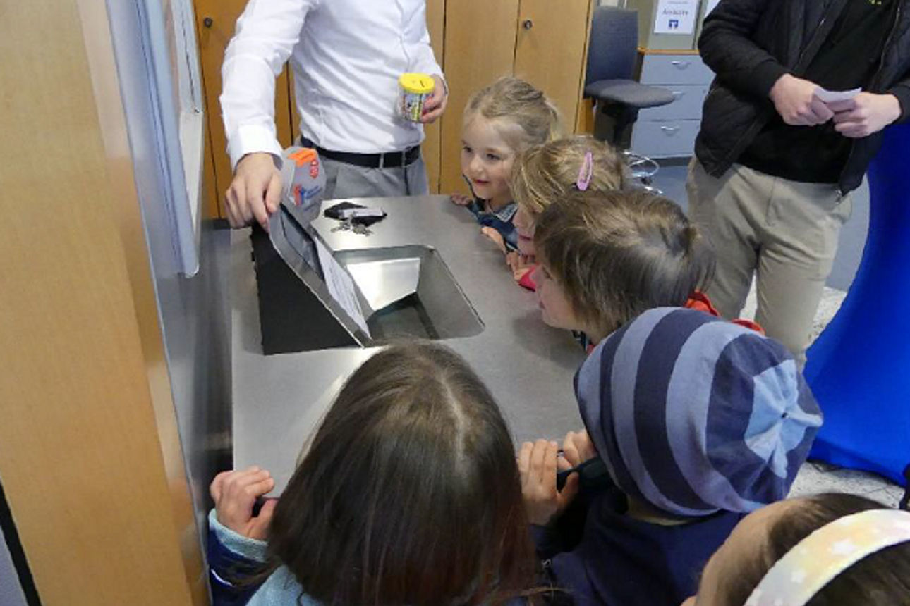 Eine Gruppe von Kindern schauen sich den Kontoauszugsdrucker an. 