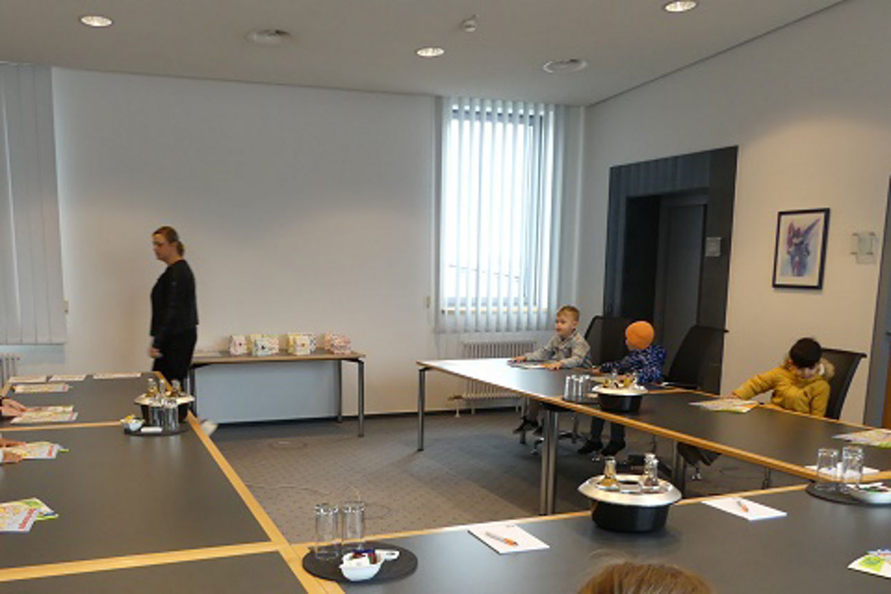 Kinder in einem Besprechungssaal wärend eine Angestellte was b erichtet.